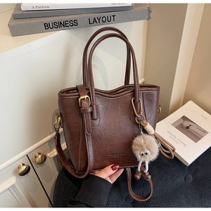 Dettaglio borsa a secchiello vintage in pelle PU marrone con pompon e tracolla regolabile