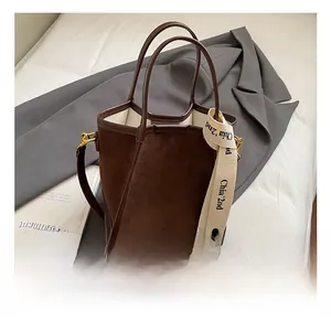 Détail du sac seau en daim marron foncé avec bandoulière large à lettres blanches et métal doré