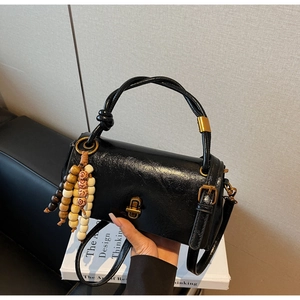 Detail of black glossy leather handbag with vintage gold twist lock and beaded tassel