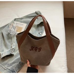 Close-up of brown canvas tote bag with red-brown webbing handles and XQG embroidery