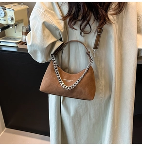 Sac demi-lune en daim marron avec chaîne argentée porté par un mannequin dans un café douillet