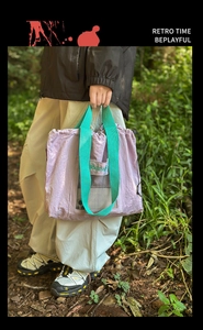 Detail of purple nylon tote bag with green handles and mesh pocket in an outdoor setting