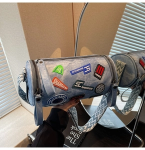 Dettaglio della borsa a cilindro in denim blu con toppe ricamate e tracolla larga