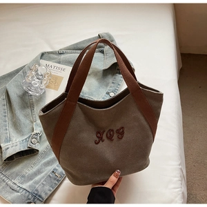 Detail of coffee brown canvas tote bag featuring embroidered XQG lettering and woven handles
