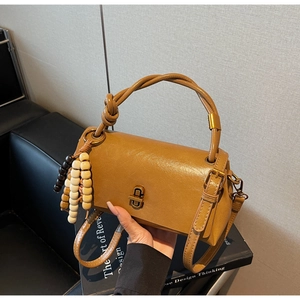 Detail of tan leather crossbody bag with braided handle and gold twist lock closure