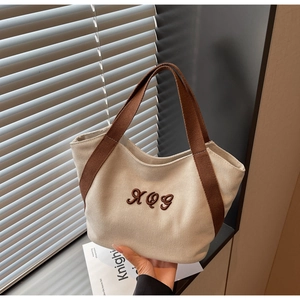 Detail of canvas tote bag featuring premium brown webbing handles and XQG embroidery