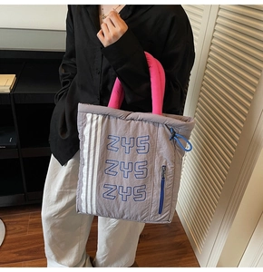 Detail of grey quilted tote bag with pink handles, side zipper and white stripes