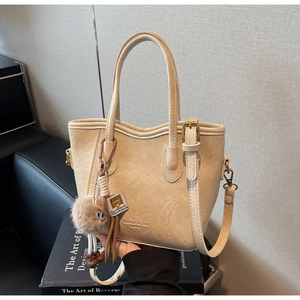 Dettaglio di una borsa tote in ecopelle beige con ciondolo di peluche e tracolla