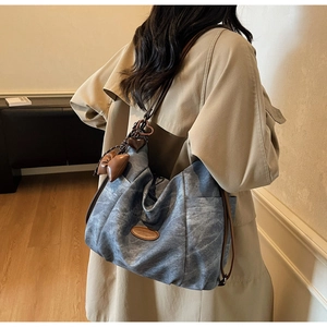 Detail of vintage denim tote bag featuring leather straps and heart charm on khaki trench coat