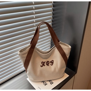 Detail of white canvas tote bag featuring brown ribbon handles and 3D letter embroidery