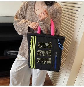 Detail of black puffer tote bag with pink handles, yellow ZYS logos and blue zipper accents