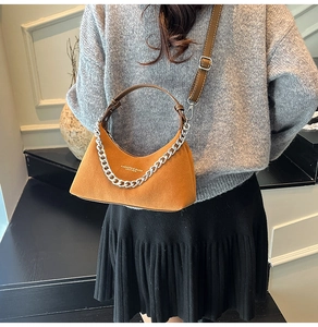 Détail d'un sac demi-lune en daim marron avec chaîne argentée porté par un mannequin