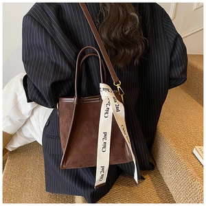 Détail d'un sac seau en daim marron avec ruban logo et finitions passepoilées en cuir