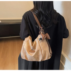 Detail of beige tote bag with dark brown adjustable strap and leather bow charm accent
