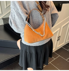 Détail d'un sac à main en daim marron avec une chaîne argentée porté par un modèle