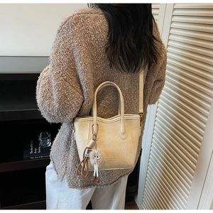 Dettaglio borsa tote in ecopelle color crema con bordo ondulato e ciondolo di peluche