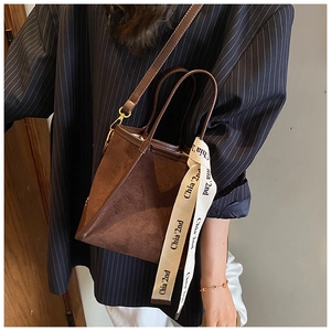 Détail d'un sac seau en daim marron avec un ruban tricoté décoratif sur la poignée