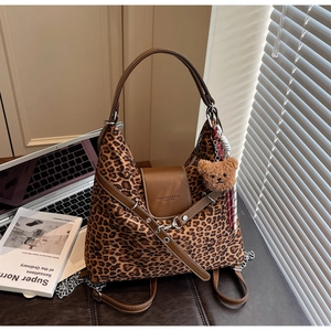 Detail of leopard print tote bag with brown leather handles and plush bear charm