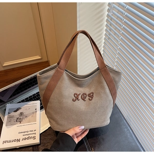 Detail of canvas tote bag with thick woven handles and embroidered logo in soft light
