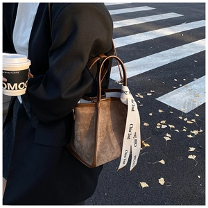 Détail d'un sac seau en daim marron avec bordure en cuir et ruban décoratif sur l'anse