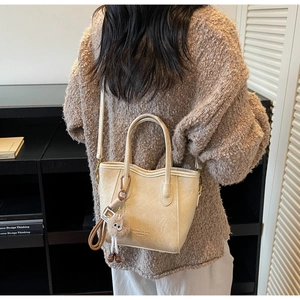 Dettaglio della borsa a secchiello beige con ciondolo di peluche e stampa sul cuoio