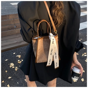 Détail du sac seau en daim marron avec garniture en cuir et ruban beige en ville