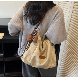 Rear view of a model wearing a beige canvas hobo bag with brown leather straps and bow