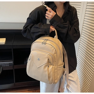 Detail of beige pebble leather backpack worn by model in a modern indoor setting