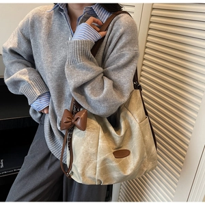 Detail of beige hobo tote bag with brown leather straps and a decorative bow charm