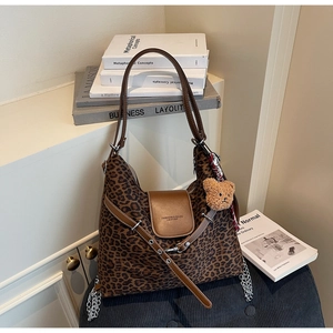 Detail of leopard print tote bag with brown leather strap and plush bear charm accent