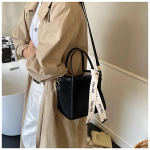 Détail d'un sac seau noir avec une bandoulière décorative porté par un mannequin