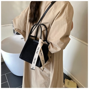Détail du sac seau noir mat avec une sangle crème lettrée pour le quotidien chic