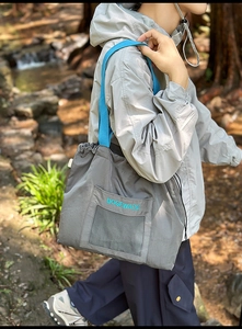 Detail of grey drawstring tote bag with blue strap and mesh pocket in outdoor forest setting