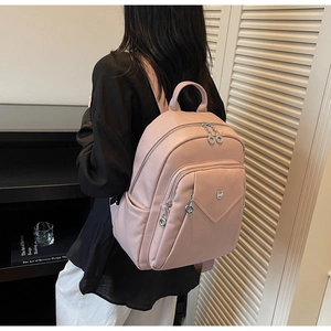 Detail view of pink pebbled leather backpack with multiple zipper pockets on a model