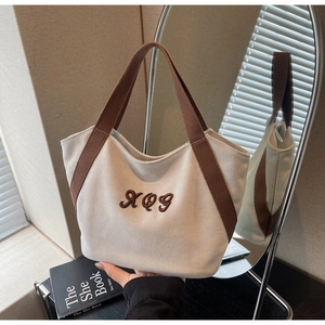 Detailed shot of beige canvas tote bag with brown handles and embroidery on a book