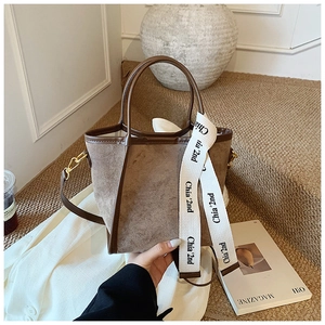 Gros plan du sac seau en daim marron avec garniture en cuir et sangle à lettres