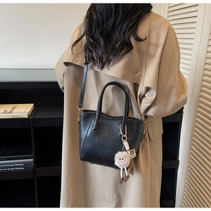 Dettaglio borsa a secchiello in pelle martellata nera con ciondolo su trench beige