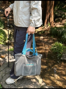 Outdoor view of dark grey nylon tote bag with blue handles and front mesh pocket