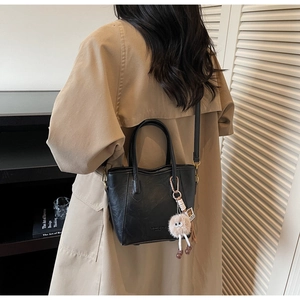 Modella che indossa una borsa a secchiello in pelle nera con charm mostriciattolo