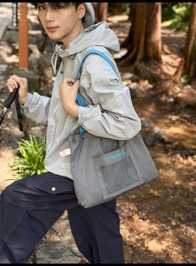 Outdoor detail showing a large dark grey tote bag with blue straps on a male model
