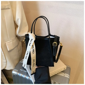Détail d'un sac seau en daim noir avec poignée en cuir et finitions métalliques dorées