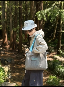 Detailed shot of grey nylon tote bag with blue straps and outdoor sun hat in a forest