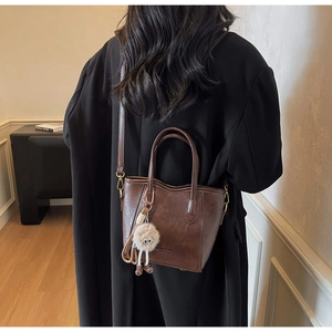 Dettaglio di borsa a secchiello vintage marrone con ciondolo su cappotto nero