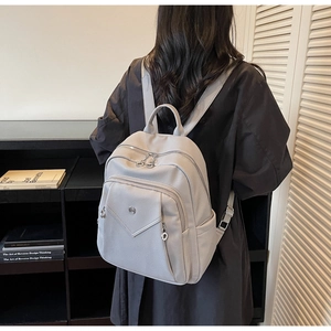 Detail view of a light gray lychee texture backpack with multiple zipper compartments