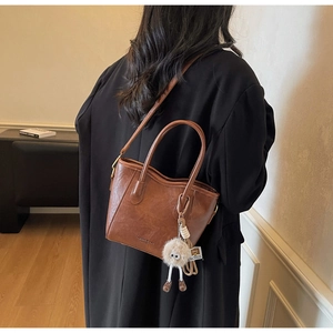 Dettaglio di una borsa a secchiello in pelle marrone con un ciondolo in peluche carino