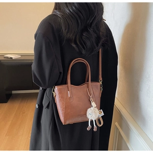 Dettaglio di una borsa tote vintage marrone con un ciondolo di peluche bianco su un cappotto
