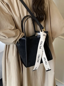 Sac seau noir en daim avec sangles en toile et bandoulière, porté sur un trench-coat classique