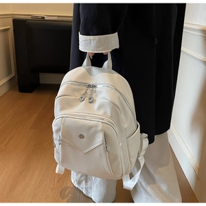 Detail of white pebbled leather backpack showing silver zippers and metal brand logo charm