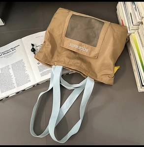 Detail of tan tote bag with mint green handles, mesh pocket, and brand logo