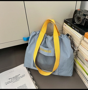 Detail of blue nylon tote bag with yellow straps, mesh pocket, and drawstring closure